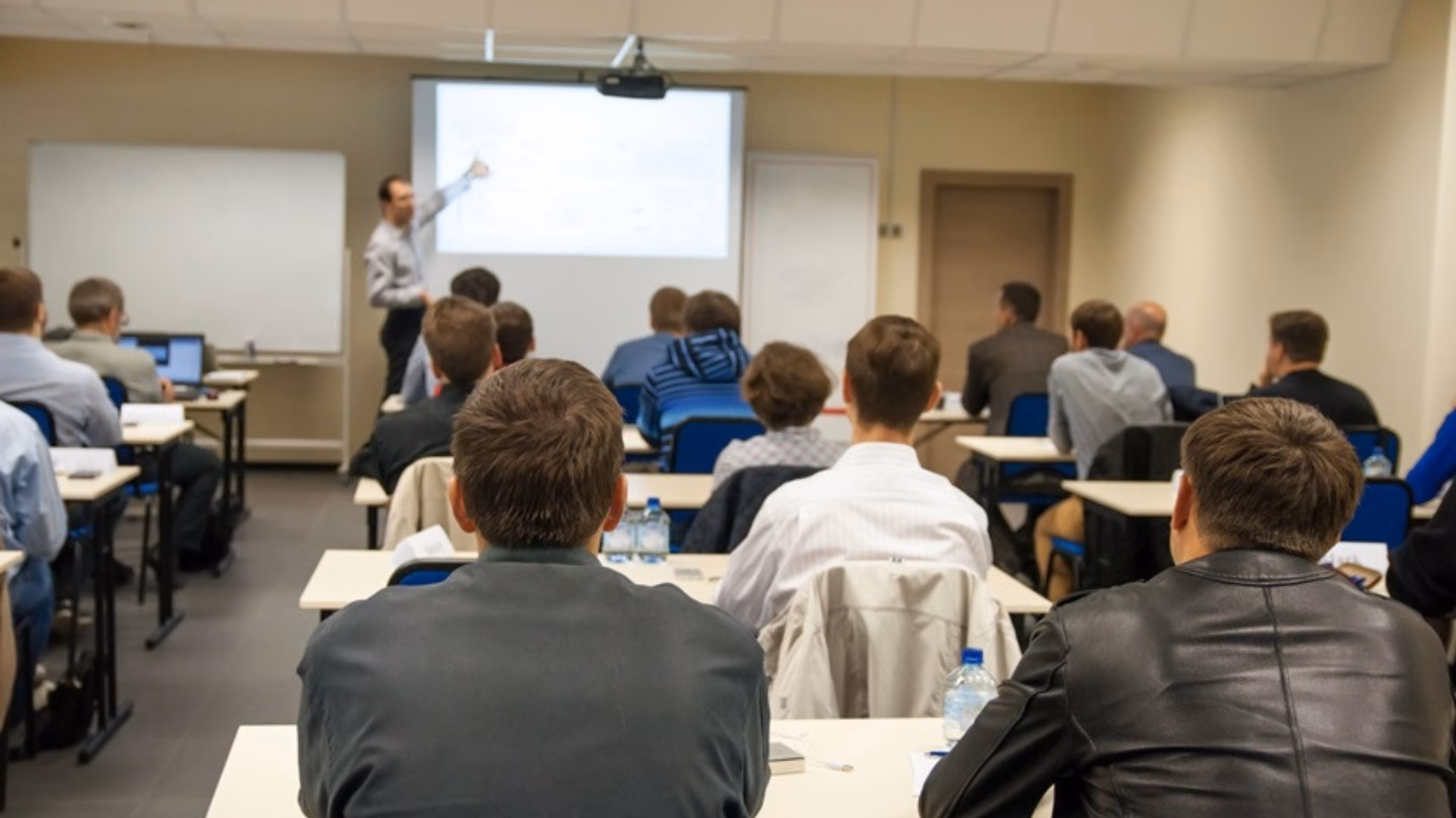 Achteraanzicht van mensen die in een klas zitten en luisteren naar een presentatie.