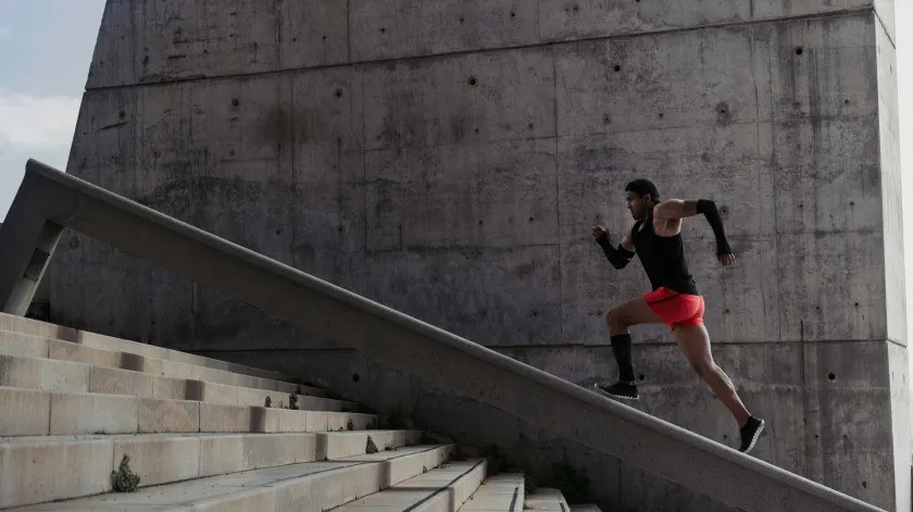 Man in sportkleding rent naar boven over een brede betonnen leuning van een trap.