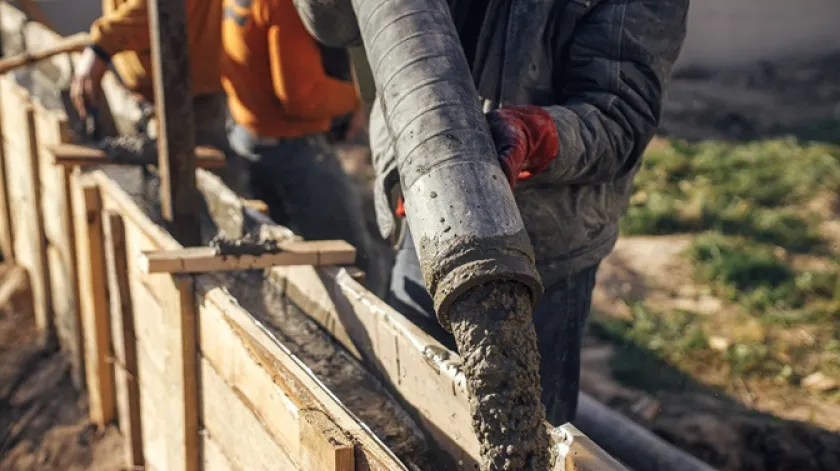 Bouwers storten beton met pompwagen in houten bekisting met versterking Werknemers gieten beton in bekisting voor fundering Bouwplaatsproces van woningbouw