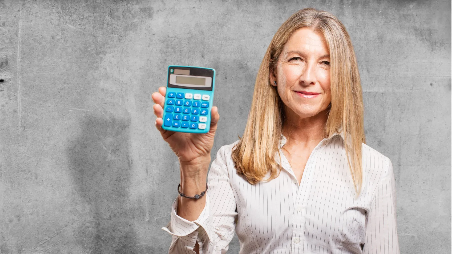 Een vrouw houdt een rekenmachine omhoog tegen een betonnen achtergrond.