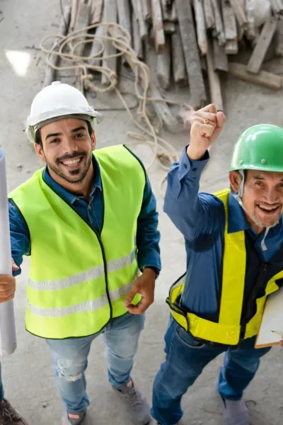 Een team van vier ingenieurs met veiligheidshesjes en helmen juicht.