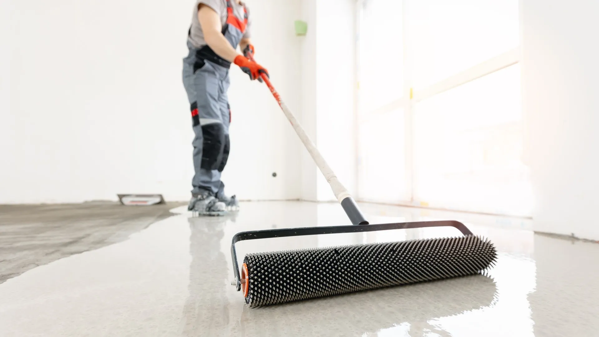 Medewerkers bewerkt een nieuwe betonnen dekvloer beton met een naaldrol