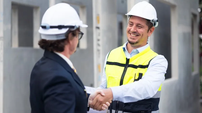 Twee medewerkers met helm schudden elkaar de hand op een bouwplaats