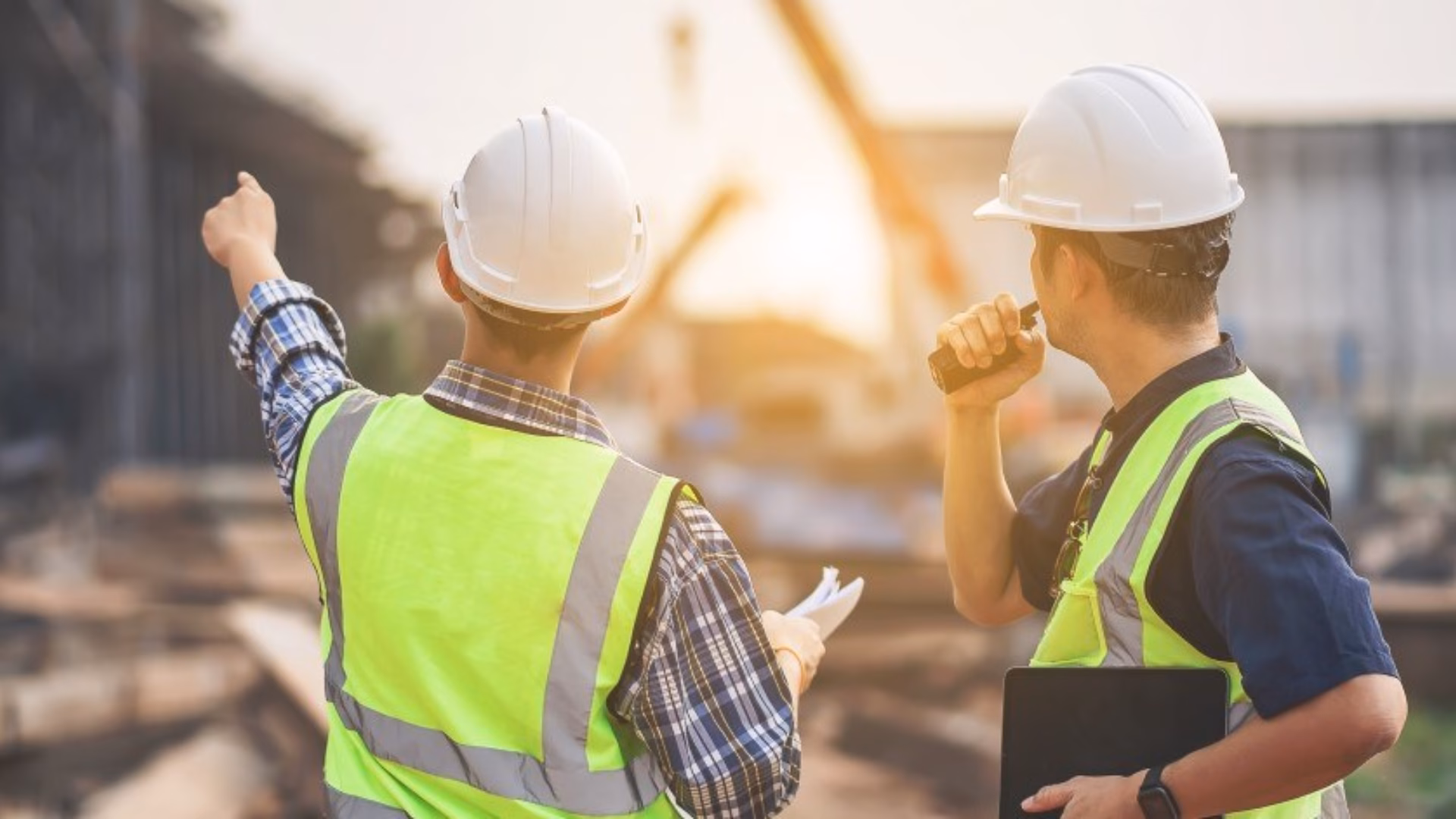 Twee ingenieurs in gele hesjes en met witte helmen inspecteren een bouwplaats