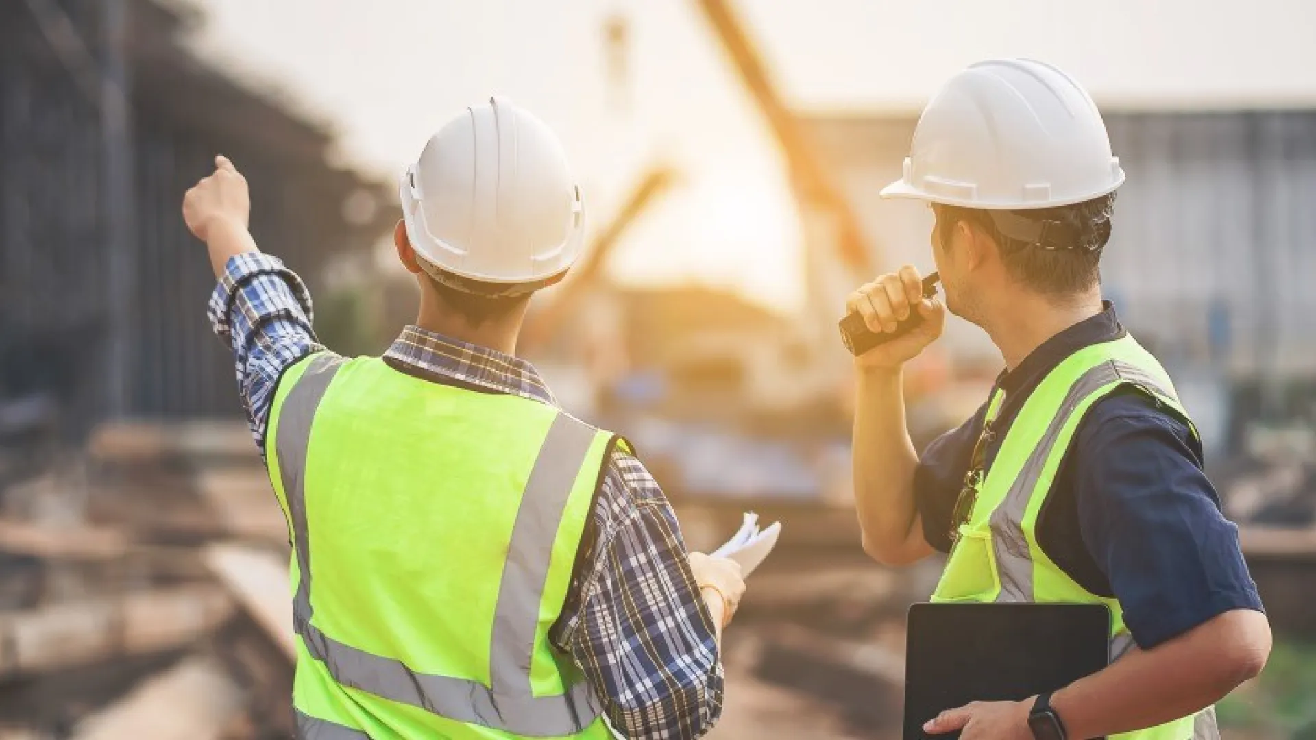 Twee ingenieurs in gele hesjes en met witte helmen inspecteren een bouwplaats