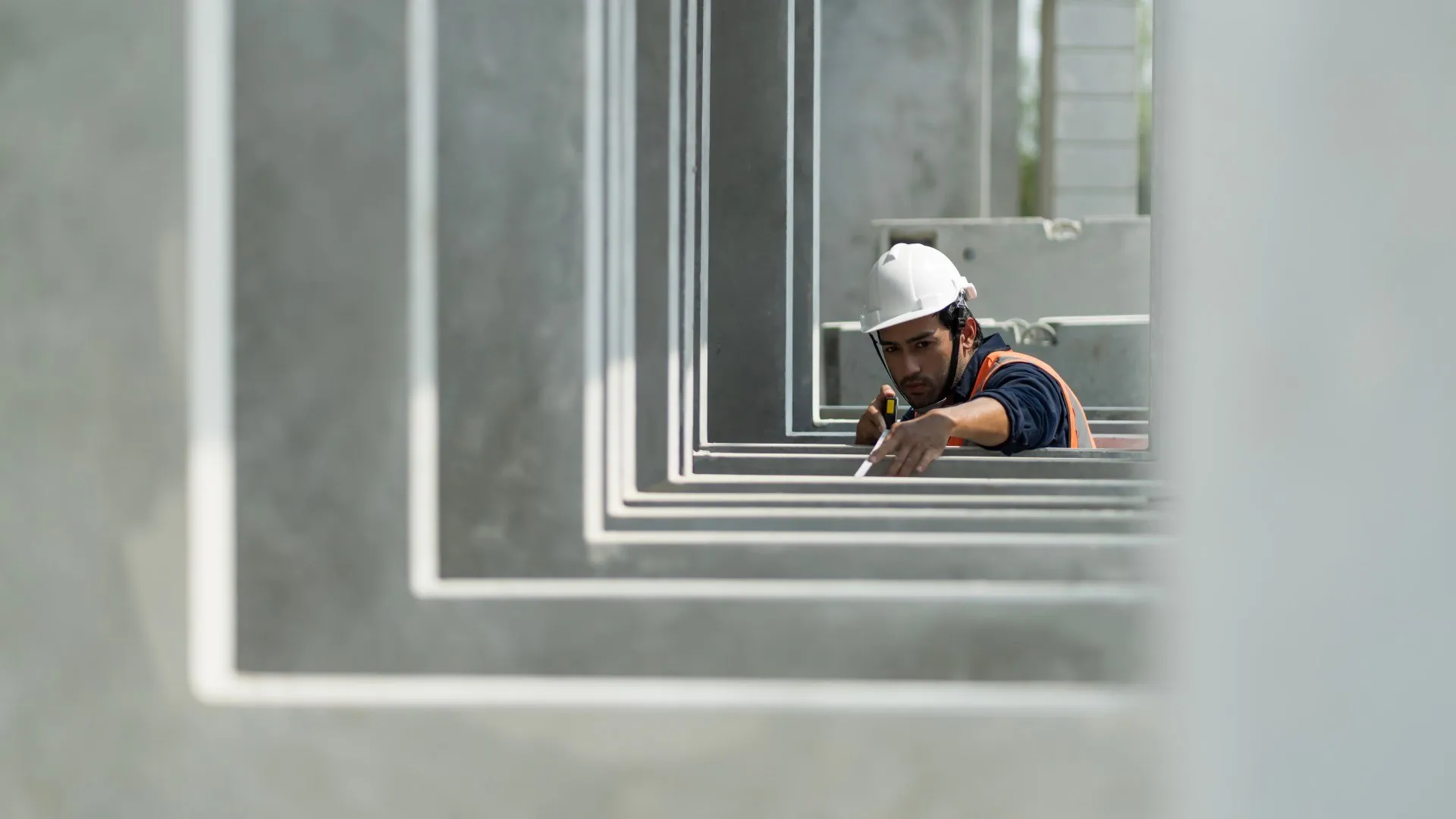 Een bouwvakker met een oranje hesje en witte helm inspecteert prefab betonelementen