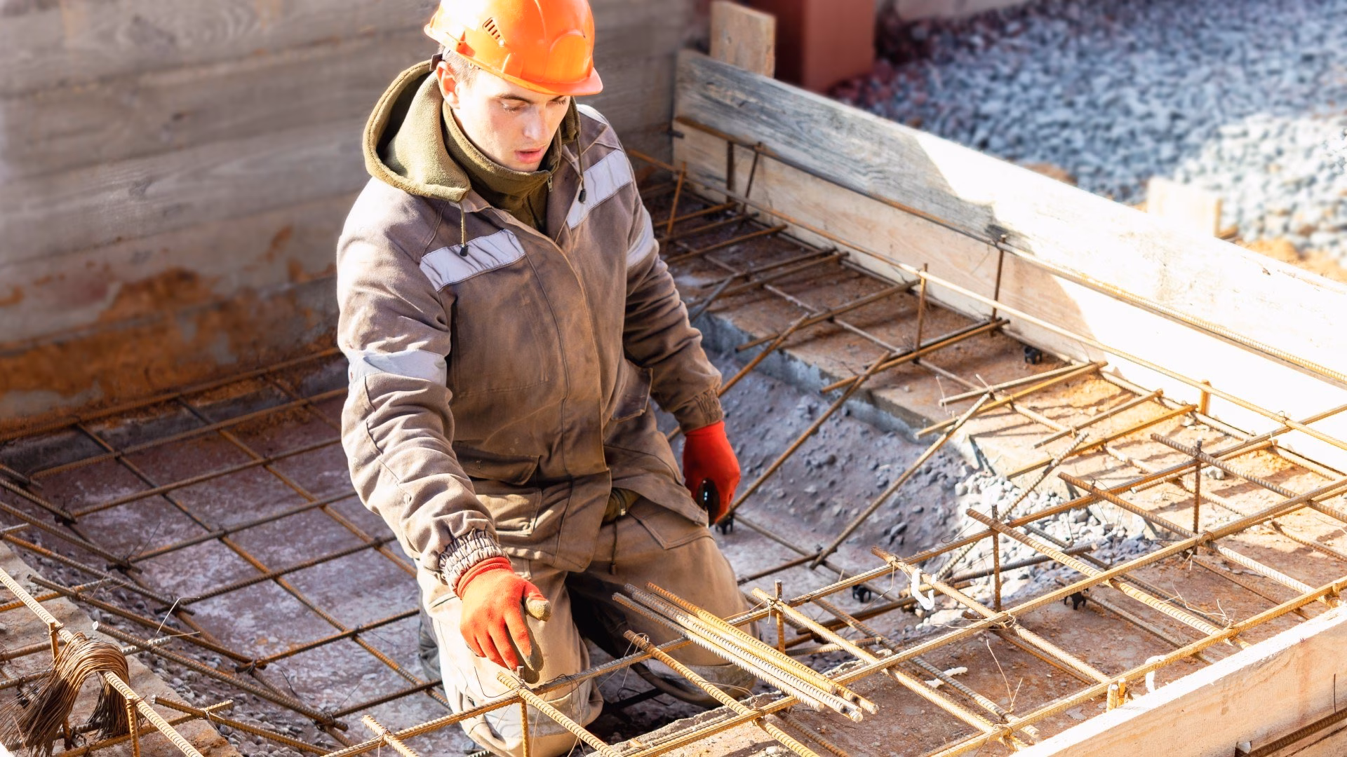 Een bouwvakker met een oranje helm en handschoenen werkt aan de stalen draden van wapening
