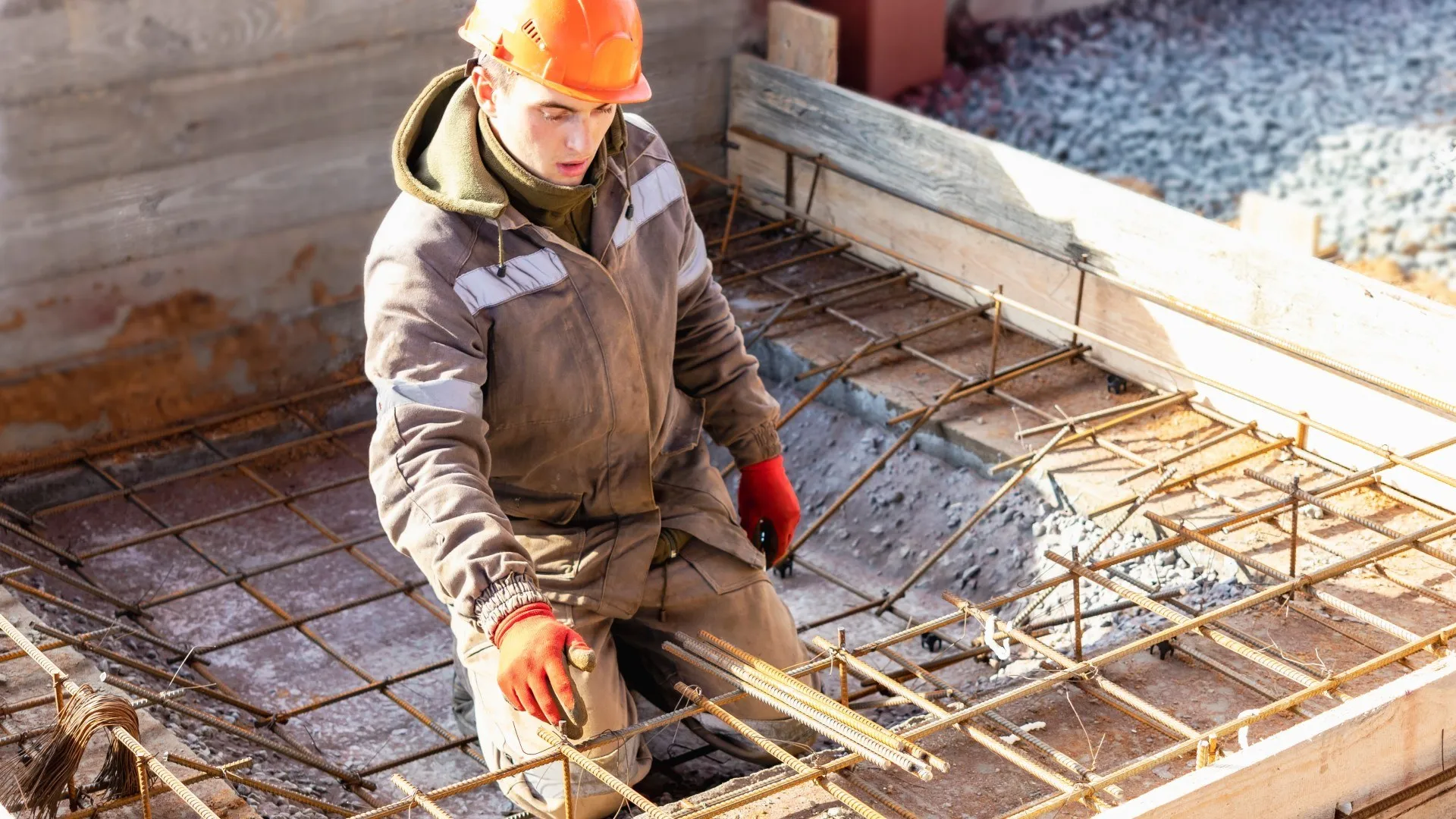 Een bouwvakker met een oranje helm en handschoenen werkt aan de stalen draden van wapening