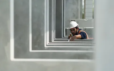 Een bouwvakker met een oranje hesje en witte helm inspecteert prefab betonelementen