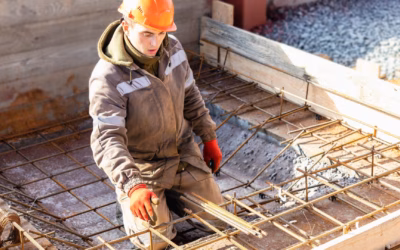 Een bouwvakker met een oranje helm en handschoenen werkt aan de stalen draden van wapening