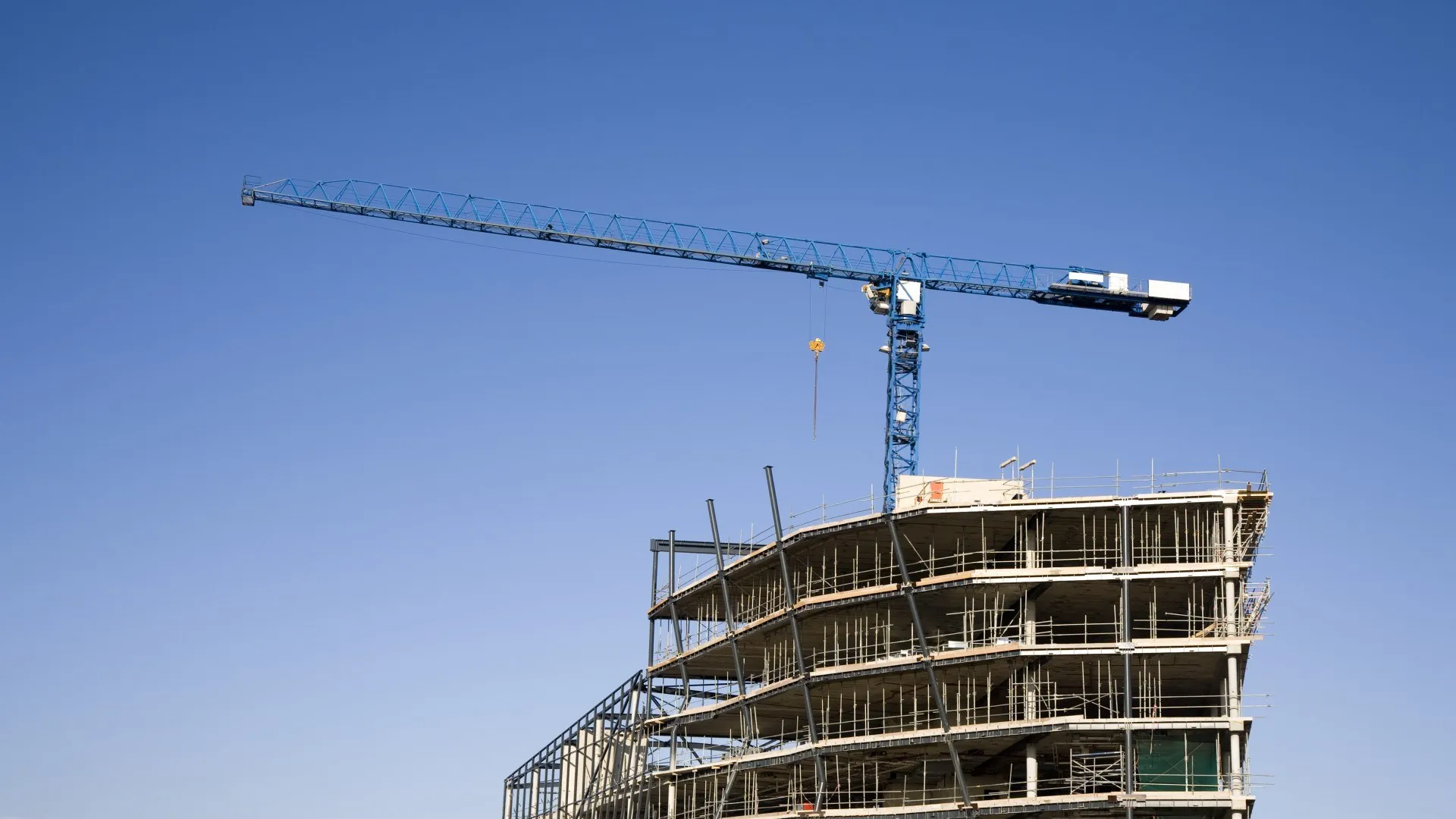 Bouwkraan steekt tegen een blauwe lucht uit boven een gebouw in aanbouw.