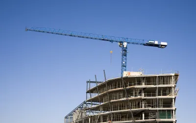 Bouwkraan steekt tegen een blauwe lucht uit boven een gebouw in aanbouw.