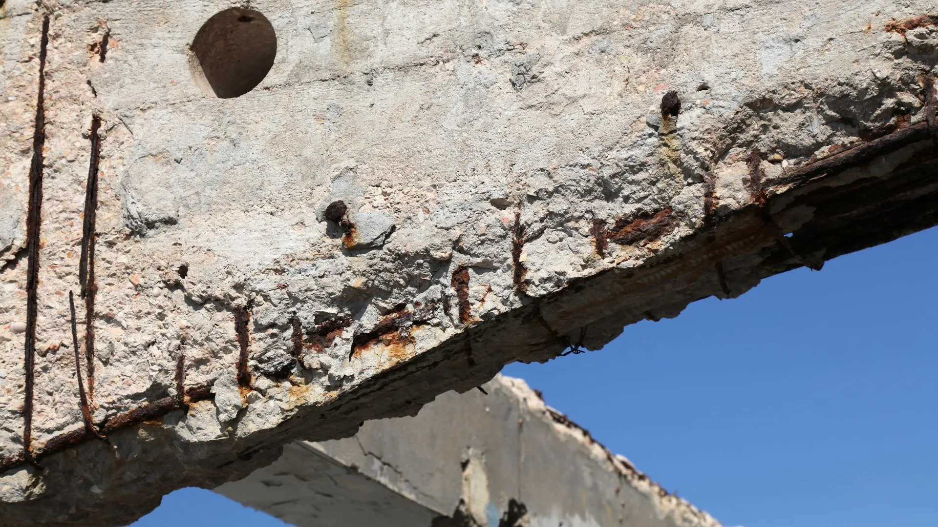 Beton is afgedrukt in een constructie aan zee onder invloed van chloriden, de roestende wapening is zichtbaar.